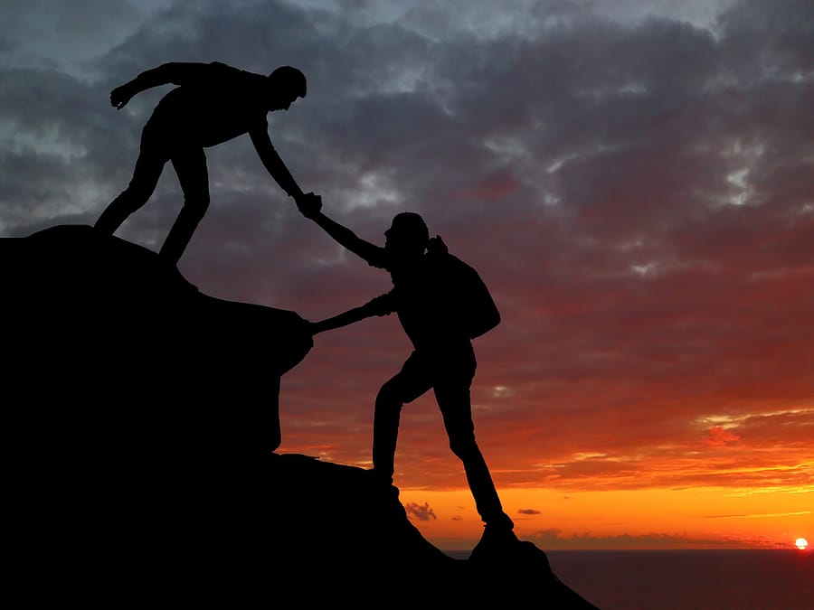 Homens se ajudando a escalar montanha dando as mãos
